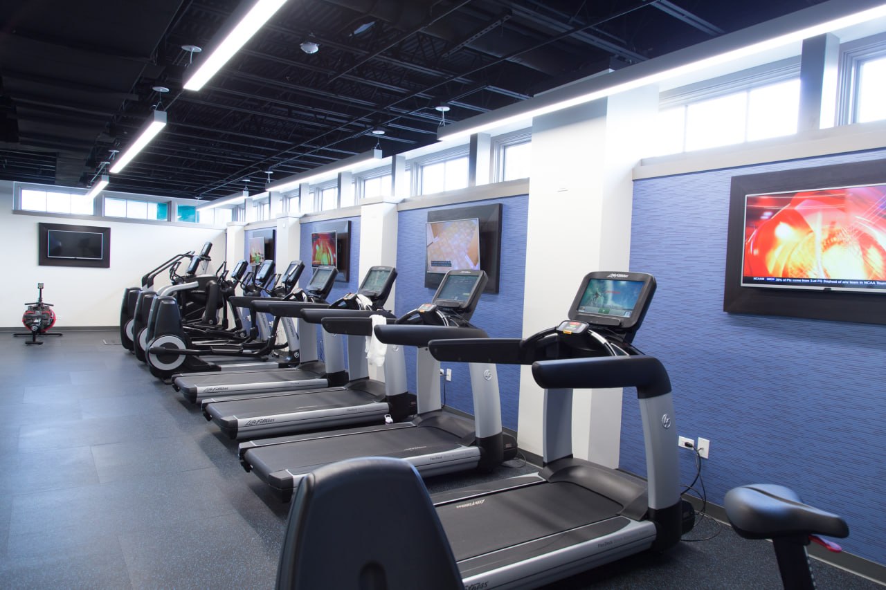 Modern fitness center with row of treadmills and touch screens